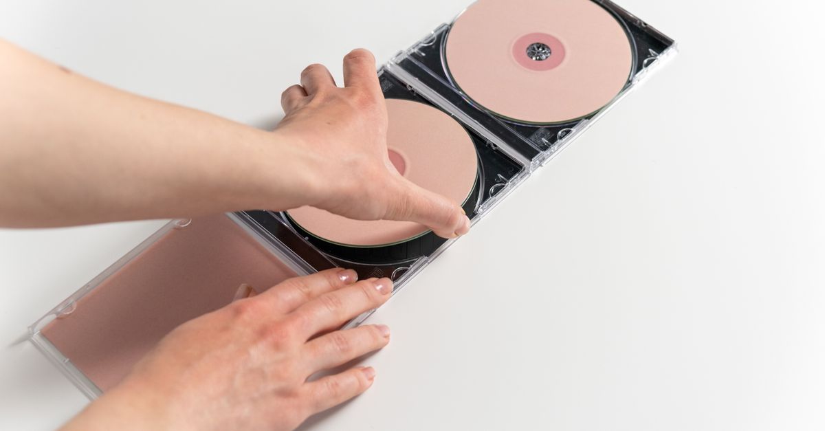 Close-up of hands holding and arranging pink compact discs in a jewel case on a white background.